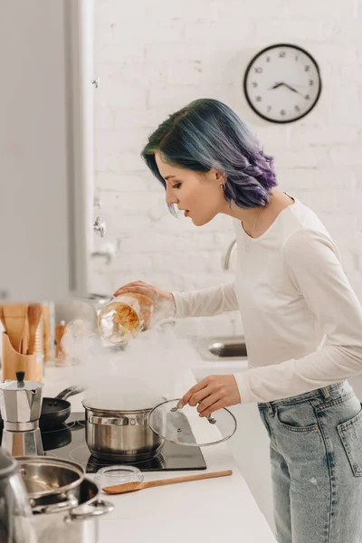 Selective focus of girl with colorful hair putting pasta in pan with steam near kitchen stove — Stock Photo