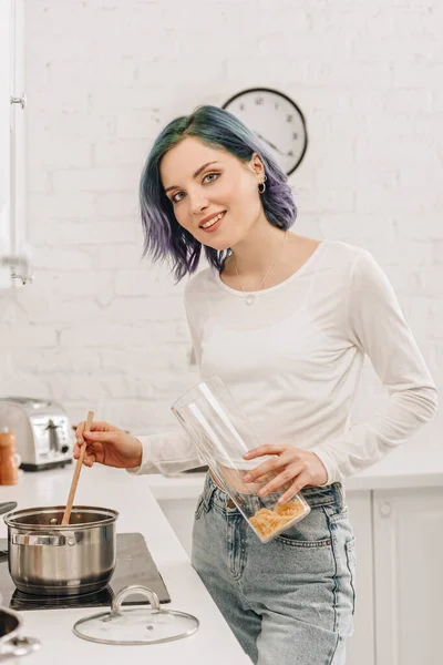 Focus selettivo della ragazza con i capelli colorati sorridenti, guardando la fotocamera e preparando la minestra in cucina — Foto stock