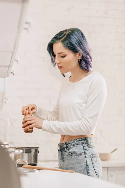 Selective focus of girl with colorful hair holding salt mill above pan on kitchen — Stock Photo