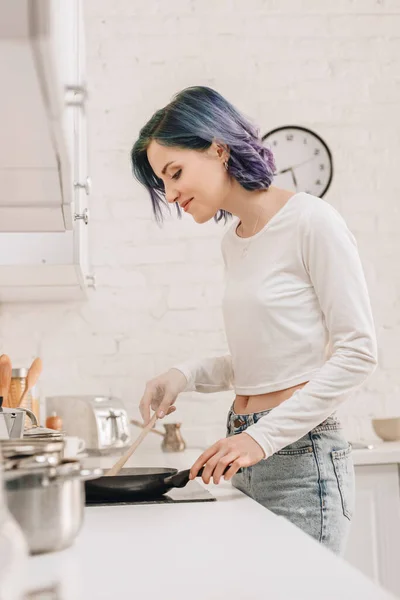 Concentration sélective de la fille aux cheveux colorés préparer la nourriture avec spatule sur poêle dans la cuisine — Photo de stock