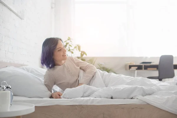 Mujer con el pelo colorido sonriendo y acostado en la cama en el dormitorio - foto de stock