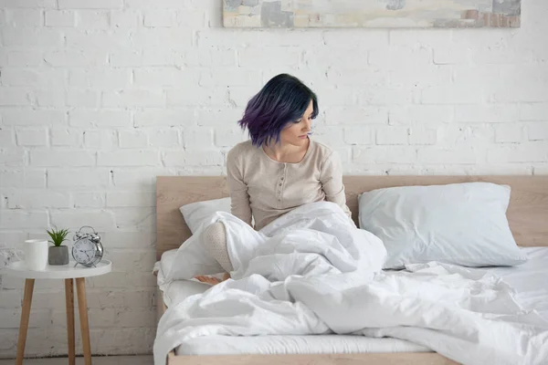 Attraktive Frau mit bunten Haaren auf Bett neben Couchtisch im Schlafzimmer — Stockfoto