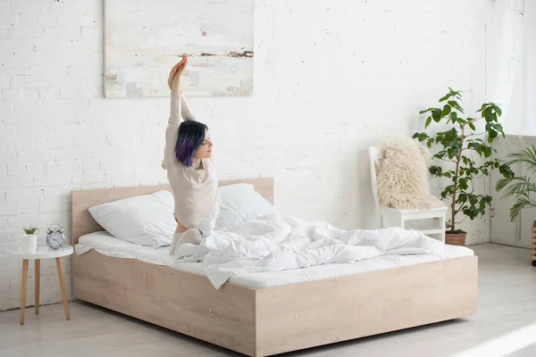 Belle femme aux cheveux colorés qui s'étire sur le lit dans la chambre — Photo de stock