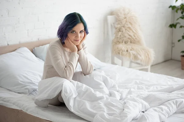 Mulher com cabelo colorido sorrindo e olhando para a câmera na cama no quarto — Fotografia de Stock