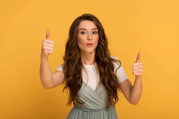 Beautiful surprised spring woman showing thumbs up isolated on yellow — Stock Photo