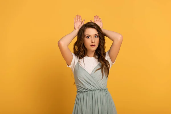 Funny girl in making bunny ears on yellow — Stock Photo