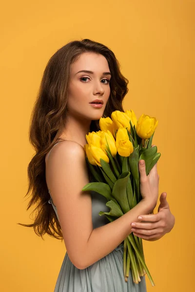 Mulher atraente em vestido de primavera segurando buquê de flores de tulipa isolado no amarelo — Fotografia de Stock