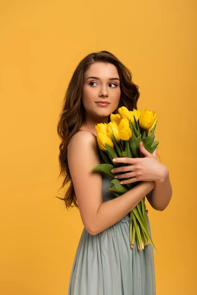 Hermosa mujer sonriente en vestido de primavera celebración ramo de flores de tulipán aislado en amarillo - foto de stock