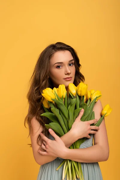 Hermosa chica en vestido de primavera celebración ramo de flores de tulipán aislado en amarillo - foto de stock