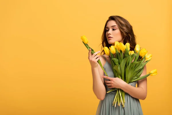 Belle fille en robe de printemps tenant des fleurs de tulipes isolées sur jaune — Photo de stock