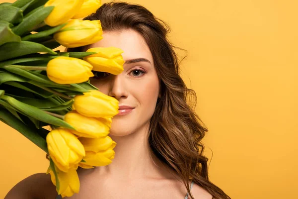 Niña sonriente sosteniendo flores de tulipán aisladas en amarillo - foto de stock