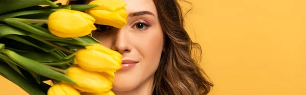 Panoramic shot of smiling girl holding tulip flowers isolated on yellow — Stock Photo