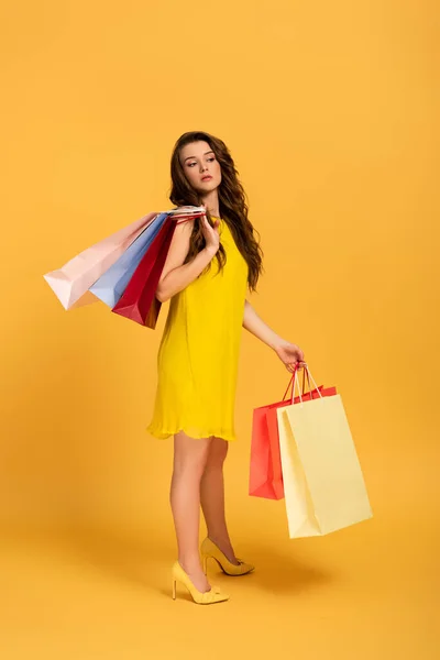 Beautiful girl in spring dress holding shopping bags on yellow — Stock Photo