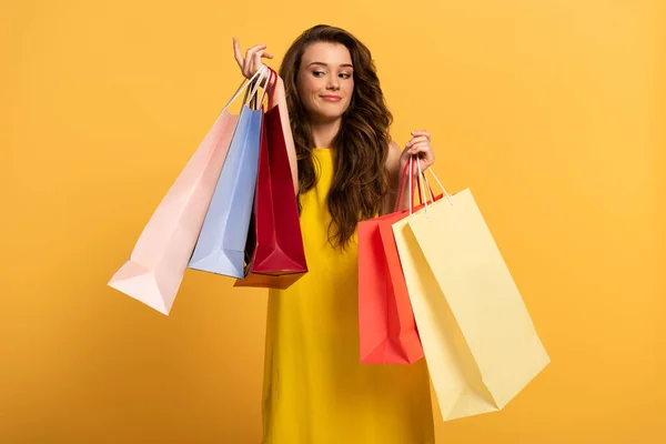 Bela menina sorridente no vestido de primavera segurando sacos de compras no amarelo — Fotografia de Stock