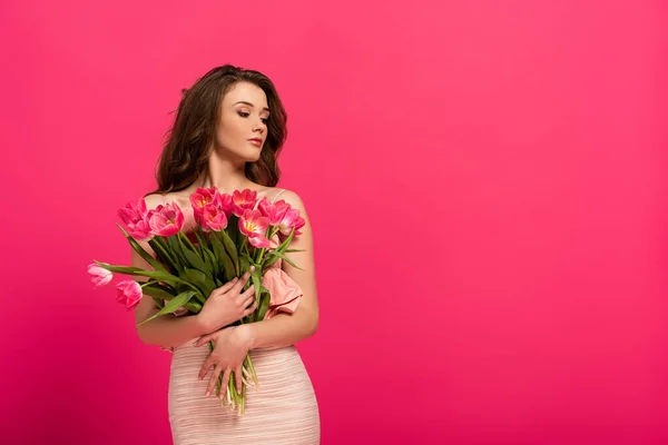 Belle fille en robe élégante tenant bouquet de tulipes de printemps isolé sur rose — Photo de stock