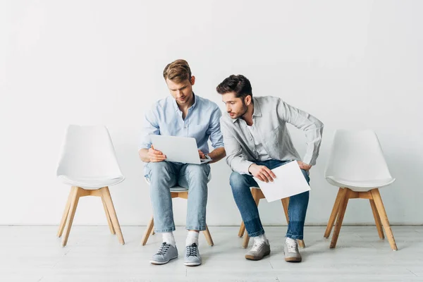 Due uomini con curriculum e laptop in attesa di un colloquio di lavoro sulle sedie in ufficio — Stock Photo