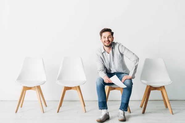 Homme souriant avec CV regardant la caméra tout en étant assis sur la chaise dans le bureau — Photo de stock