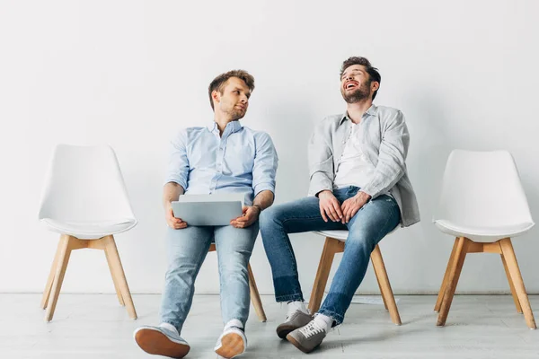 Man with laptop looking at laughing candidate on chair while waiting for job interview in office — Stock Photo