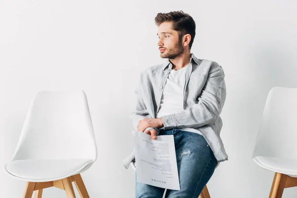 Hombre guapo sosteniendo curriculum vitae mientras está sentado en la silla en la oficina - foto de stock