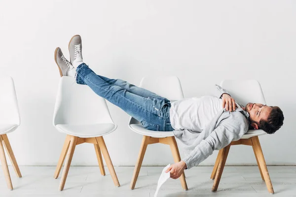 Side view of tired employee with resume lying on chairs in office — Stock Photo