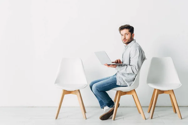 Seitenansicht des Kandidaten mit Laptop, der auf dem Stuhl in die Kamera schaut — Stockfoto