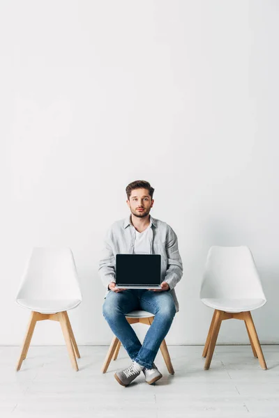 Mitarbeiter blickt in Kamera, während er Laptop mit leerem Bildschirm im Büro hält — Stockfoto