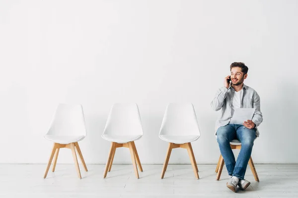 Un employé souriant parle sur son smartphone et tient son CV au bureau — Photo de stock