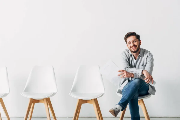 Schöner Mann lächelt in die Kamera, während er Lebenslauf und Smartphone im Büro hält — Stockfoto