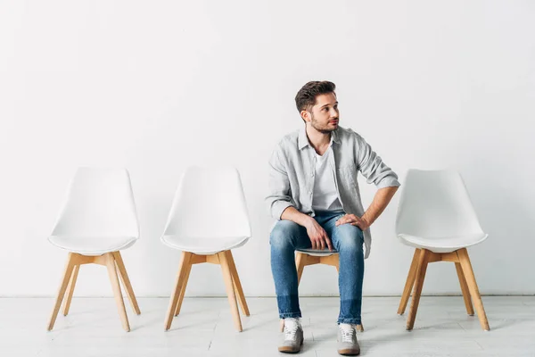 Schöner Angestellter schaut weg, während er im Büro auf Stuhl sitzt — Stockfoto