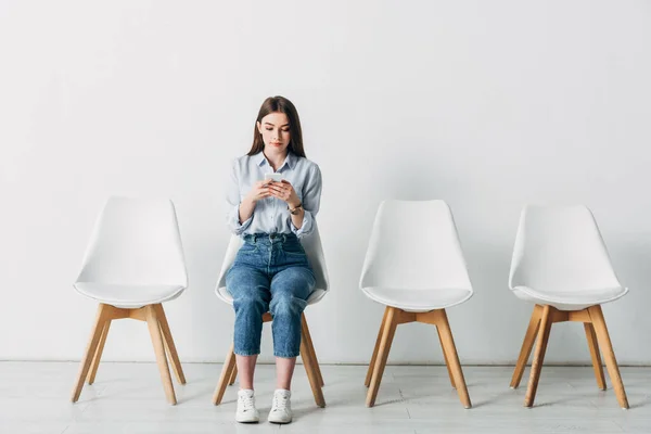 Mujer joven usando smartphone mientras espera entrevista de trabajo en la oficina - foto de stock