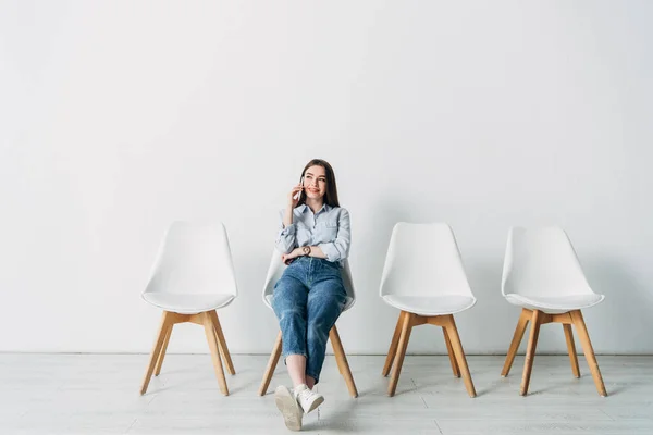 Schön lächelnde Bewerberin, die im Büro auf einem Stuhl sitzt und mit dem Smartphone spricht — Stockfoto