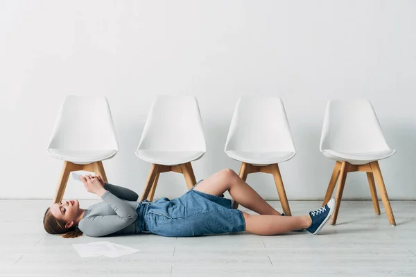 Side view of employee using smartphone near resume on floor in office — Stock Photo