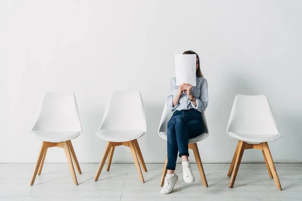 Jovem mulher cobrindo rosto com currículo enquanto espera por entrevista de emprego no escritório — Fotografia de Stock