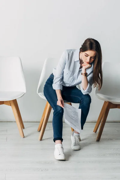 Mujer pensativa mirando currículum mientras espera entrevista de trabajo en la oficina - foto de stock