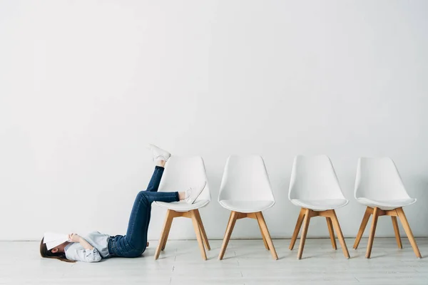 Seitenansicht des Mitarbeiters, der Gesicht mit Lebenslauf bedeckt, während er im Büro auf dem Boden liegt — Stockfoto