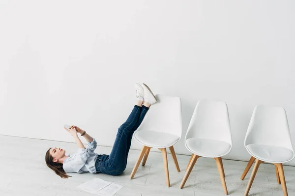 Side view of attractive employee using smartphone near resume on floor — Stock Photo