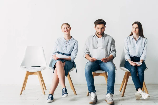 Mujer atractiva sonriendo a la cámara cerca de los empleados en la oficina - foto de stock