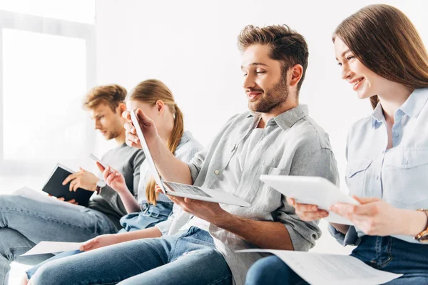 Selektiver Fokus eines lächelnden Mannes mit Laptop in der Nähe von Mitarbeitern mit Geräten im Büro — Stockfoto