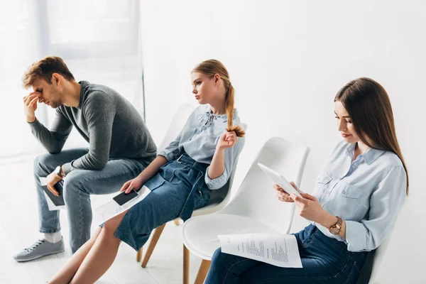 Attraktive Frau mit digitalem Tablet und Lebenslauf sitzt auf Stuhl neben Mitarbeitern im Büro — Stockfoto