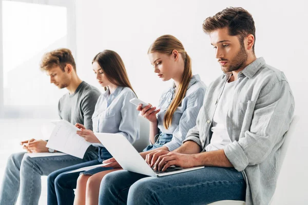 Enfoque selectivo del hombre guapo usando el ordenador portátil mientras espera la entrevista de trabajo cerca de los empleados - foto de stock