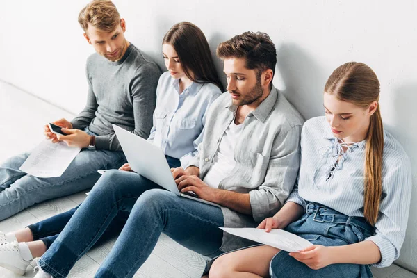 Grupo de jovens com dispositivos digitais sentados no chão à espera de entrevista de emprego — Fotografia de Stock