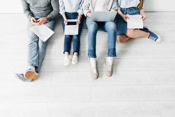 Cropped view of employees with resume and digital devices sitting on floor in office — Stock Photo