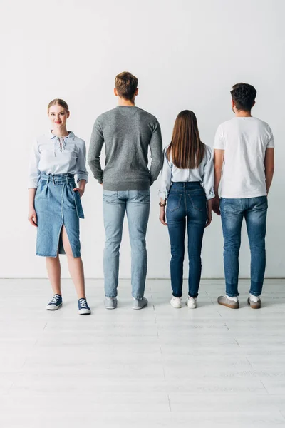 Belle employée avec la main dans la poche souriant à la caméra près des gens près du mur dans le bureau — Photo de stock