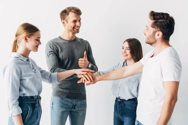 Sonriente hombre mostrando el pulgar hacia arriba mientras toma de la mano con sus compañeros de trabajo en la oficina - foto de stock