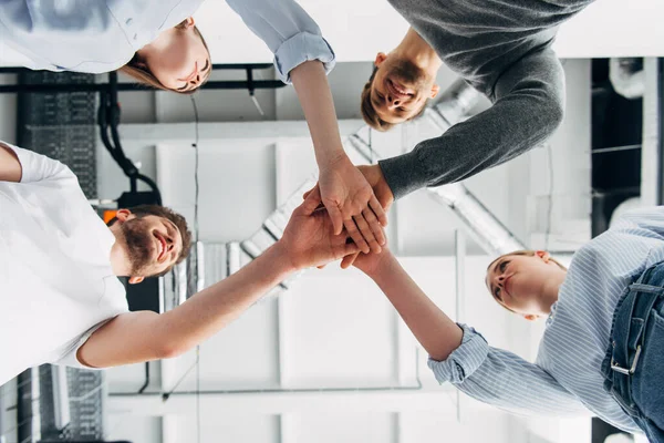 Vista inferior de compañeros de trabajo sonrientes mirándose mientras se toman de la mano en la oficina - foto de stock