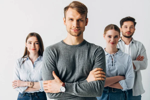 Selective focus of man smiling at camera near coworkers with crossed arms in office — Stock Photo