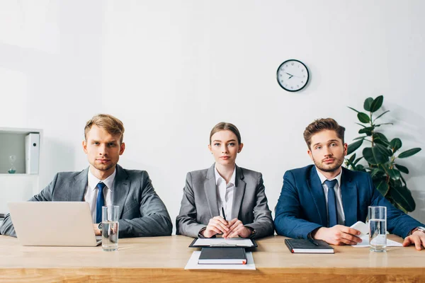 Recruiters in suits looking at camera near laptop and papers on table — Stock Photo