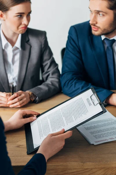 Selective focus of employee holding resume near skeptical recruiters looking at each other at table — Stock Photo