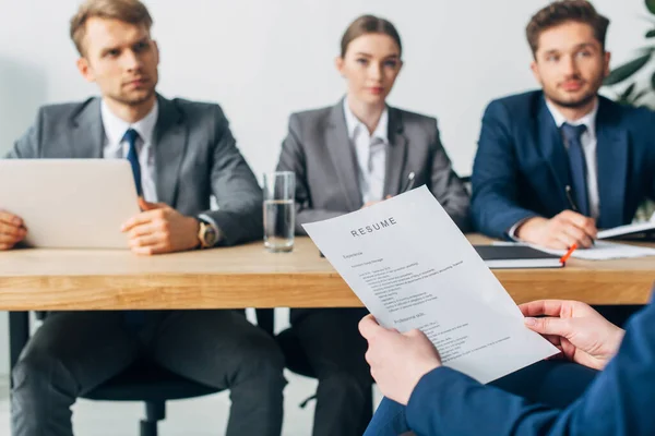 Selective focus of employee holding resume near recruiters at table in office — Stock Photo