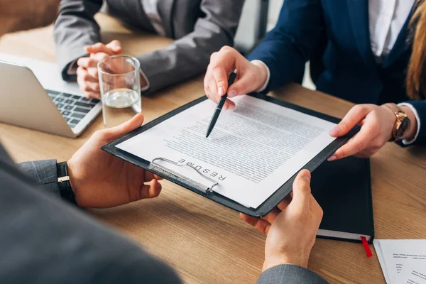 Cropped view of recruiter holding clipboard with resume near colleague and employee at table — Stock Photo